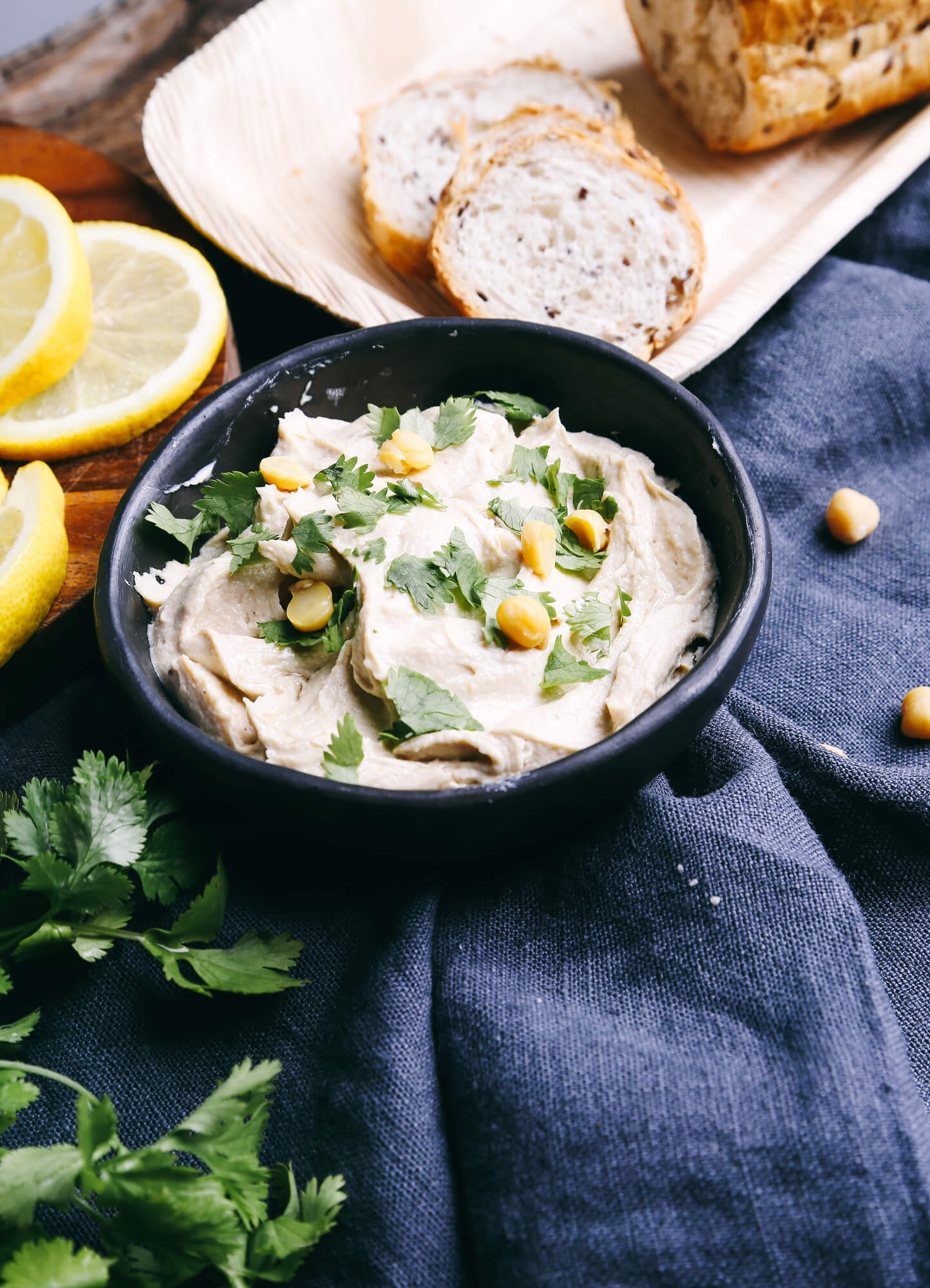 Artichoke hummus in a bowl with fresh bread, lemons, and parsley.