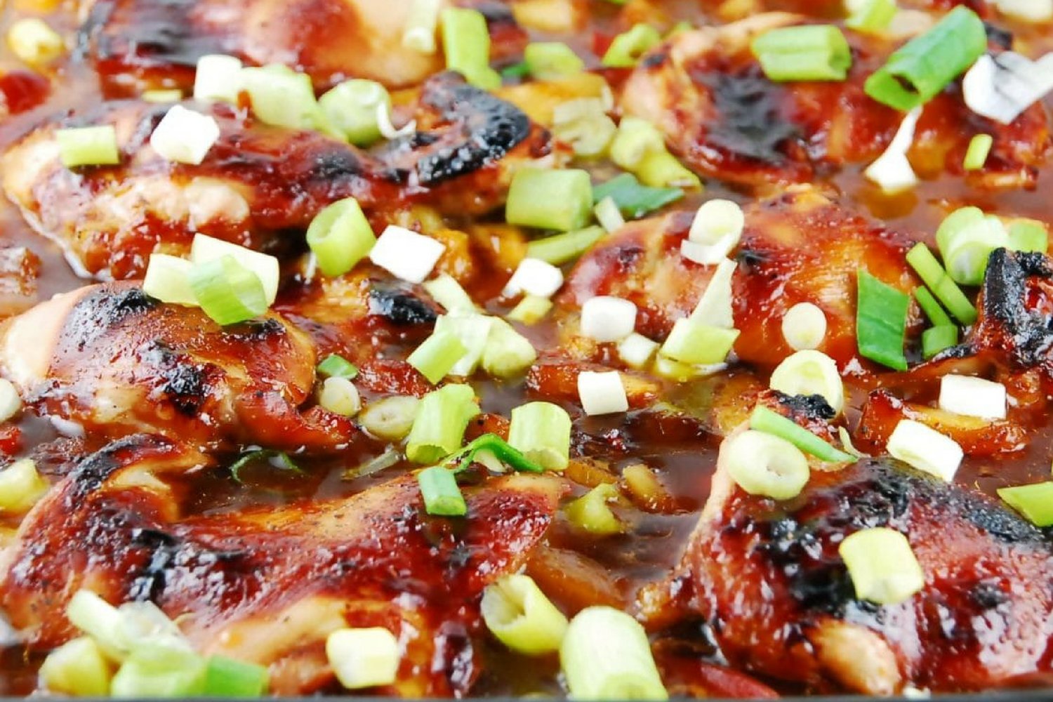 Baked teriyaki chicken in a glass dish with green onions.