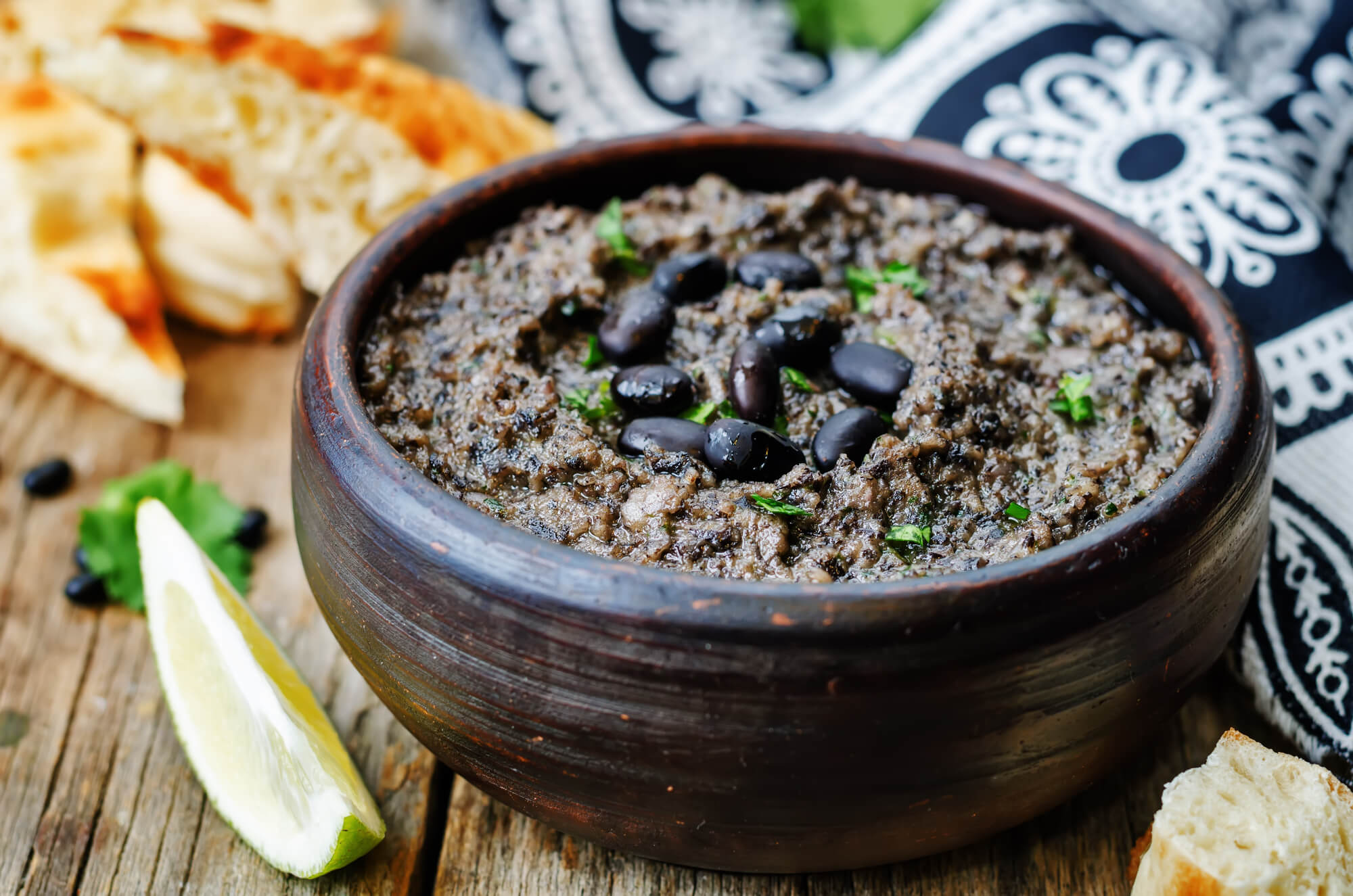 Spicy Black Bean Hummus with black beans and cilantro in a wooden bowl with bread.
