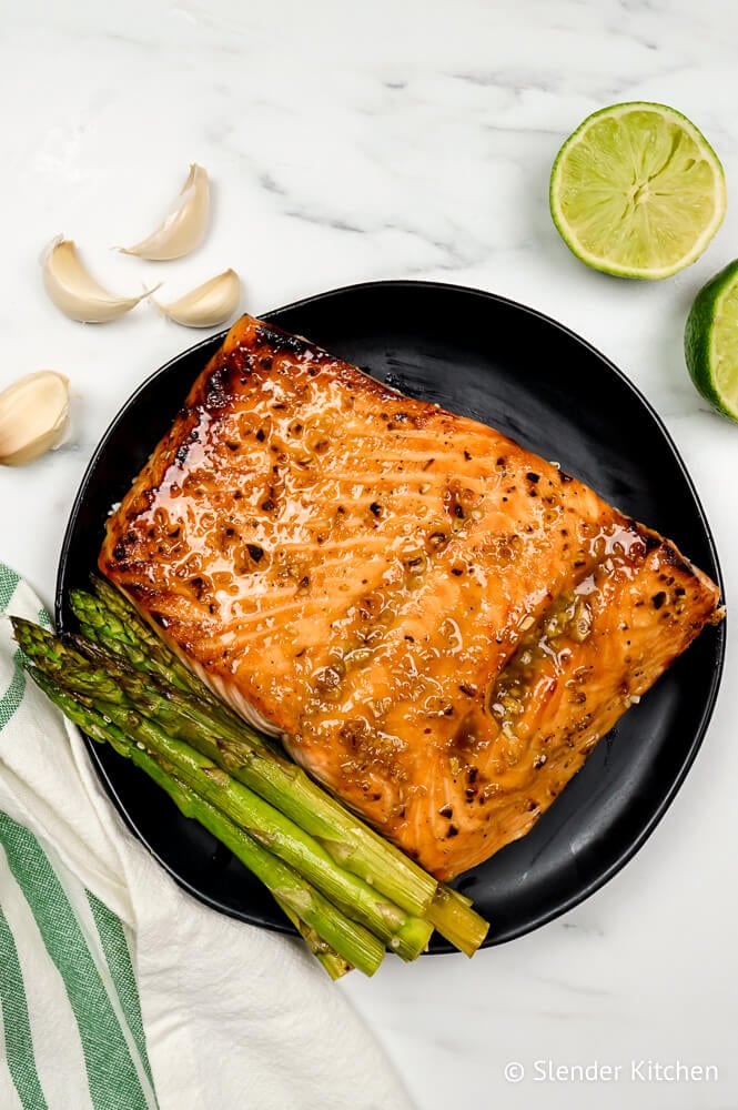 Broiled salmon on a black plate with asparagus and lime.
