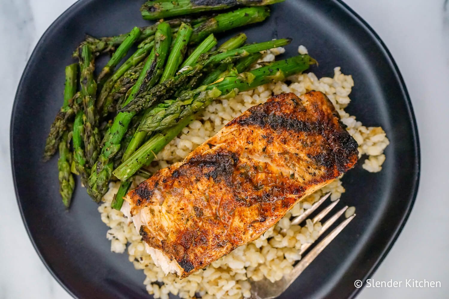 Broiled Cajun Salmon on a black plate with rice and asparagus on a white linen napkin.