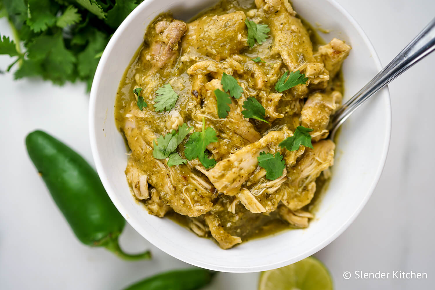 Slow Cooker Chile Verde in a bowl with cilantro and tortillas.