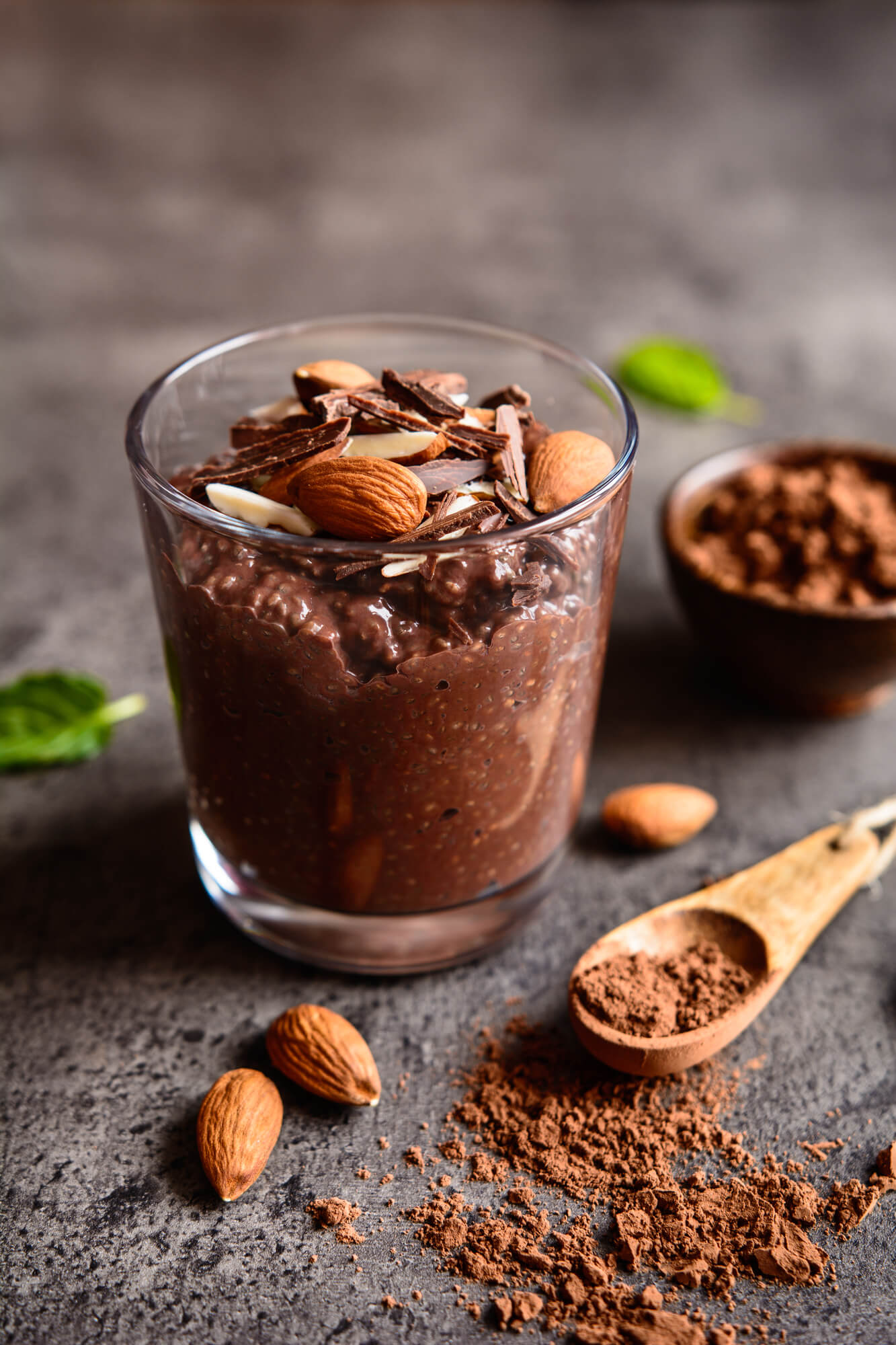 Chocolate Chia Seed Pudding in a glass with loose chia seeds and a wooden spoon.