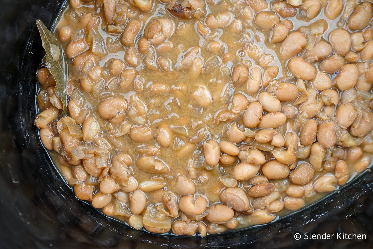 Crockpot pinto beans in a black slow cooker with bay leaf.