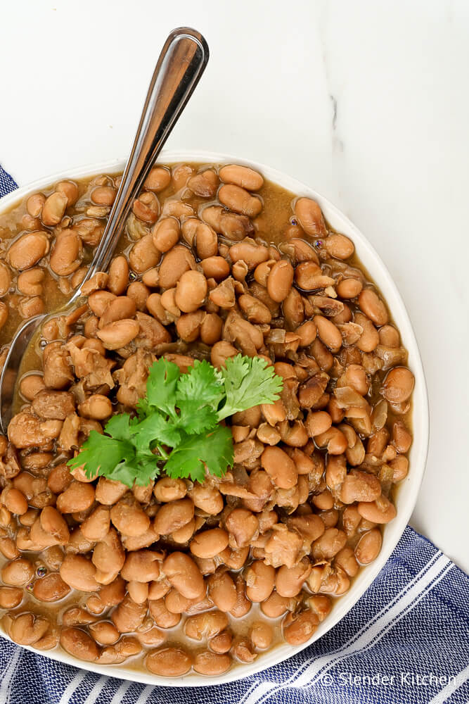 Slow cooker pinto beans in a bowl with a spoon and cilantro.