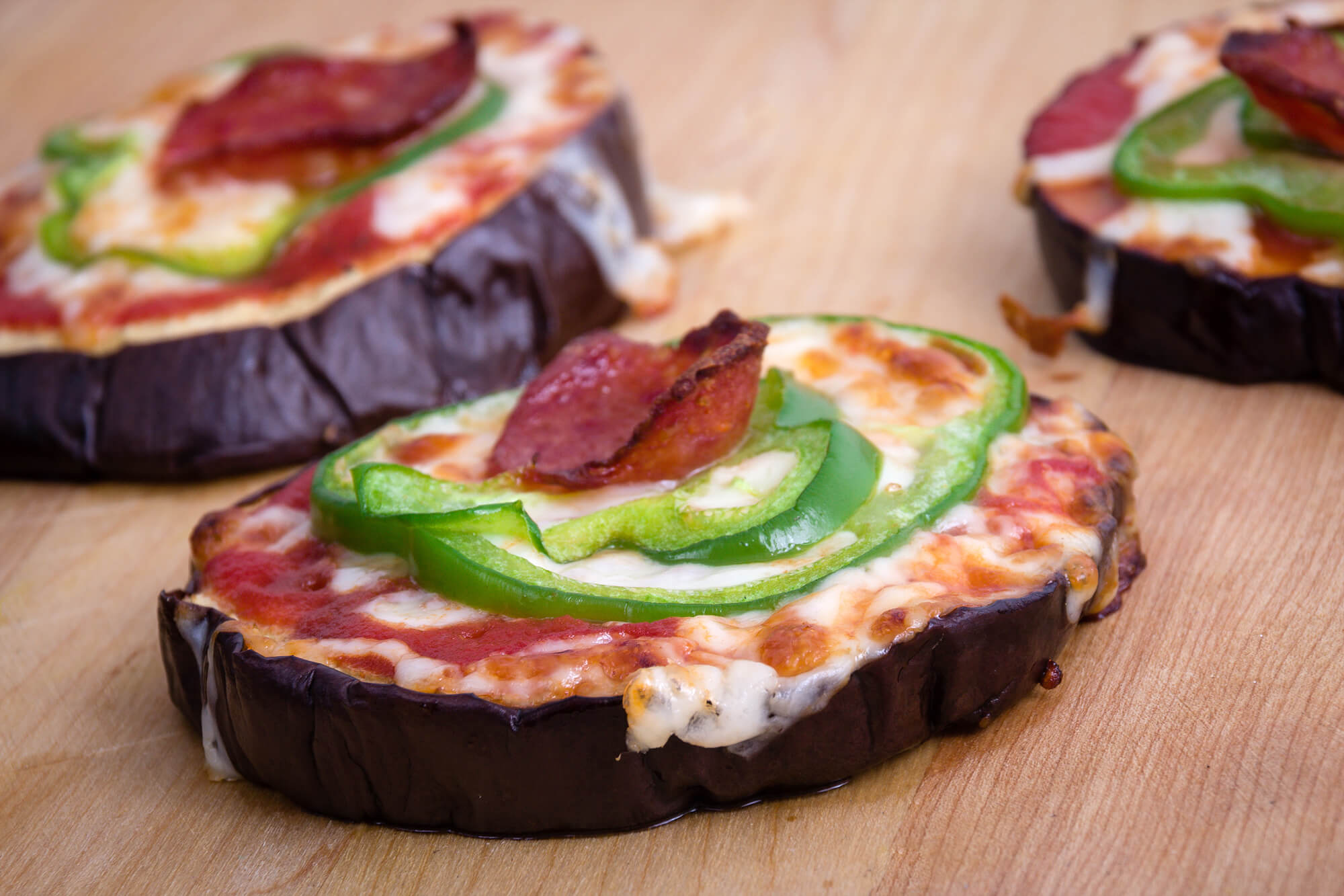 Eggplant pizza bites on a cutting board with pepperoni and green pepper.