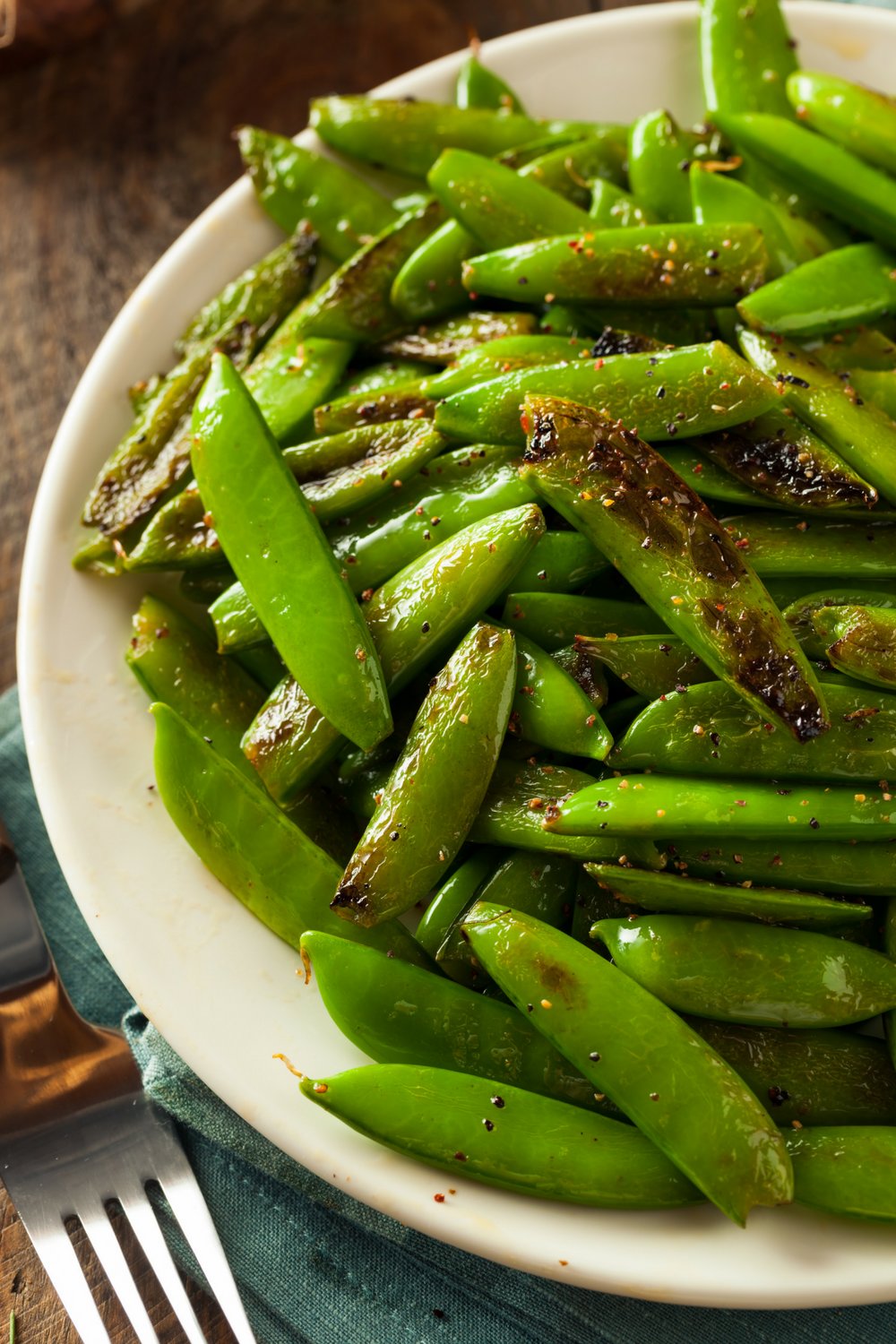 Sauteed sugar snap peas on a plate that are lightly browned.