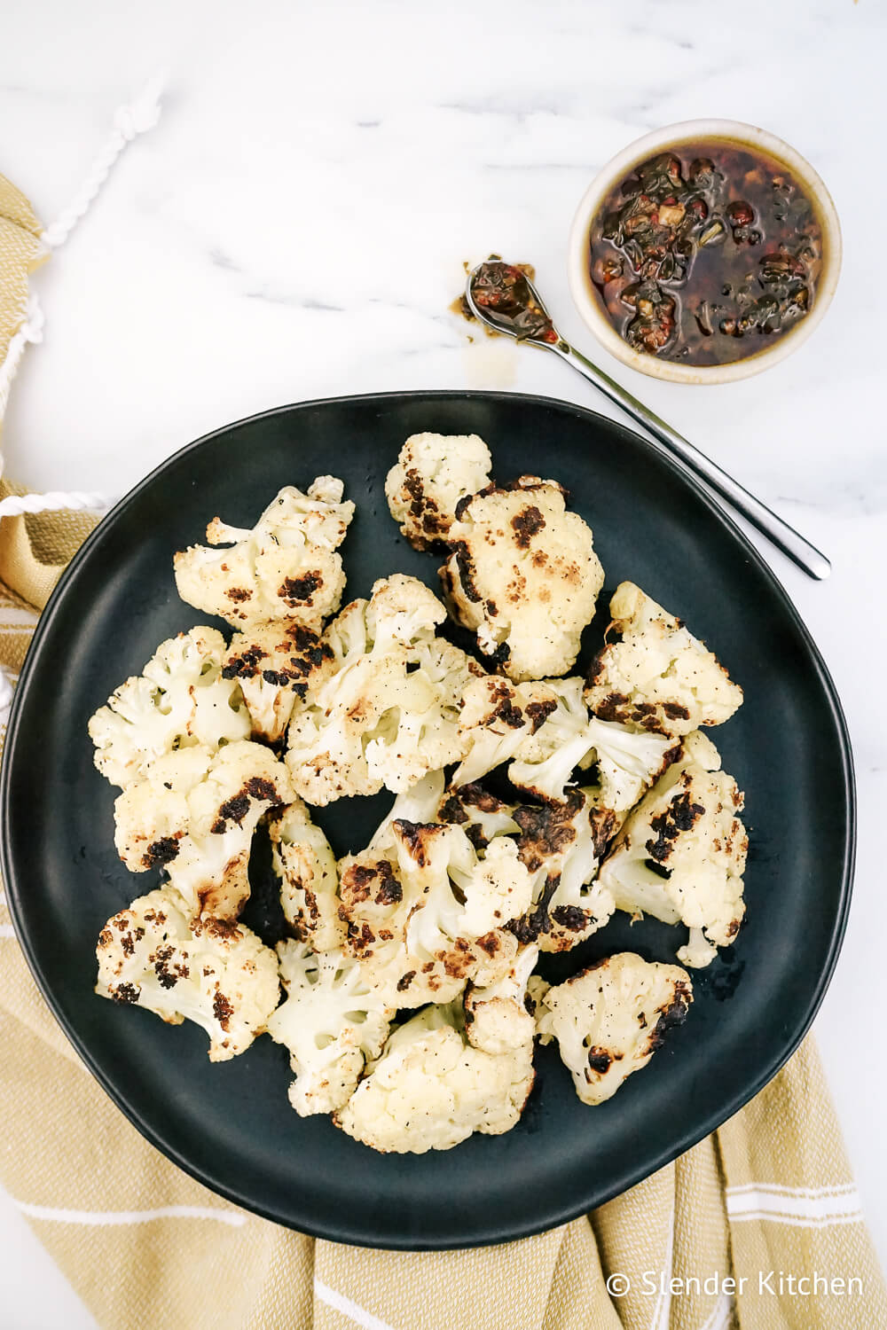 Grilled cauliflower on a black plate with chimichurri.