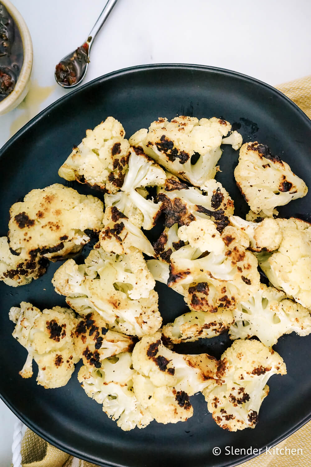 Grilling cauliflower on a white cutting board with a bowl of herbs in olive oil.