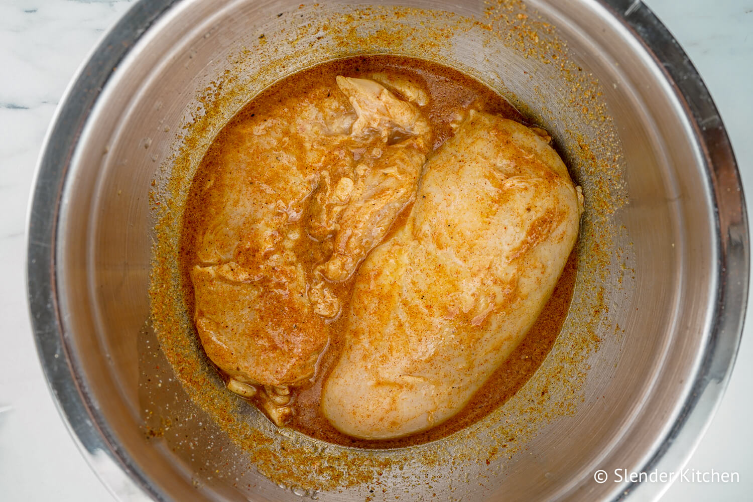 Chicken breasts in chicken taco seasoning and lime juice in a metal bowl.