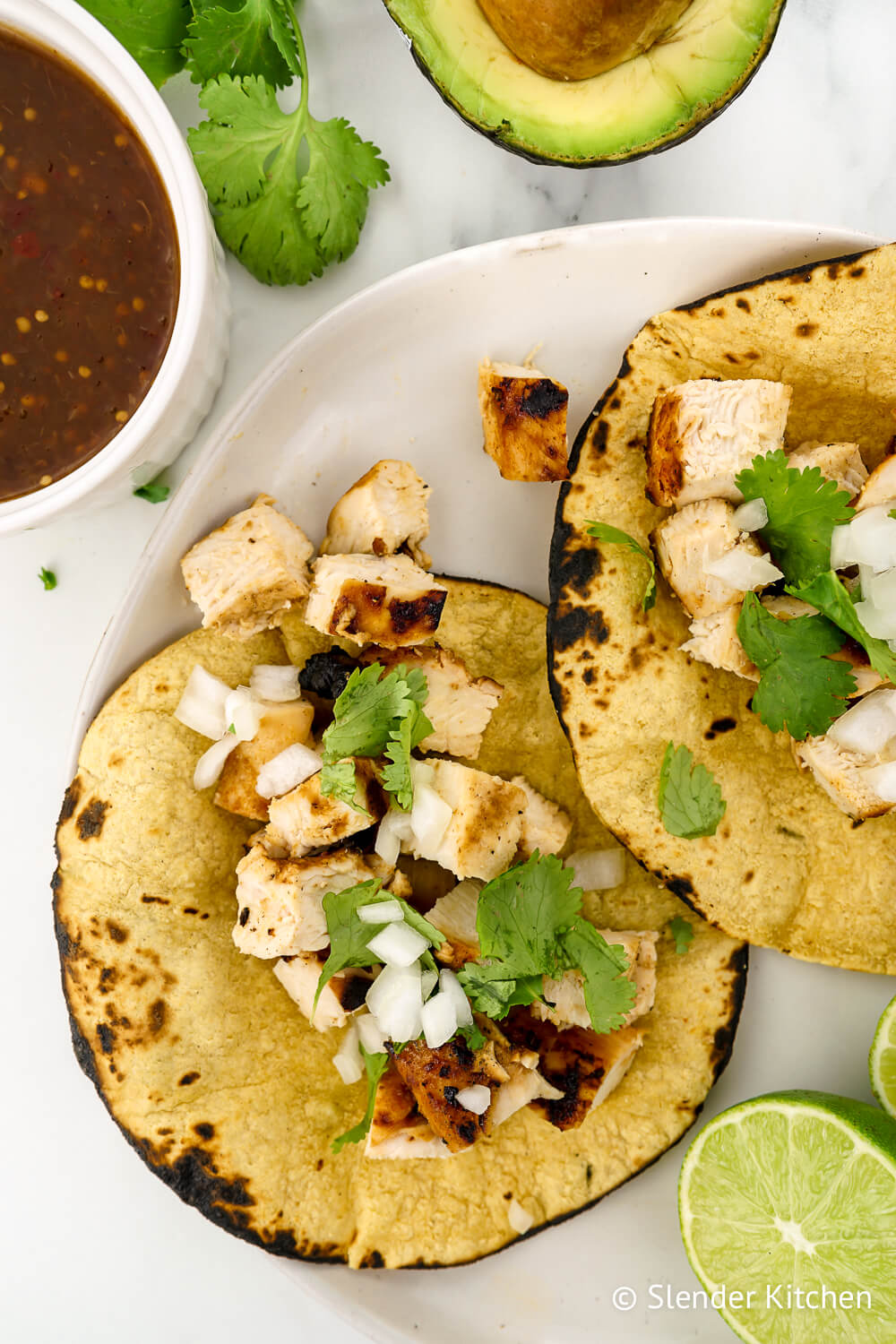 Grilled Chicken Tacos in corn tortillas with cilantro, onion, and red salsa.