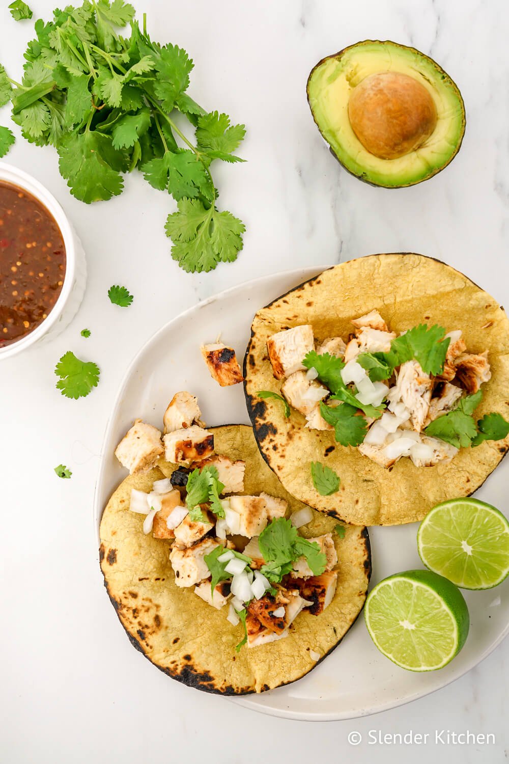Chicken tacos with cilantro and avocado on a marble background.