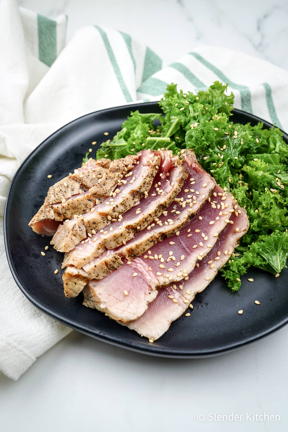 Grilled tuna steak on a black plate with kale salad and a green and white napkin.