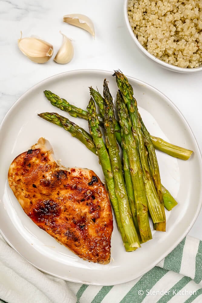 Chicken with asparagus and quinoa on a white plate with garlic on the side.