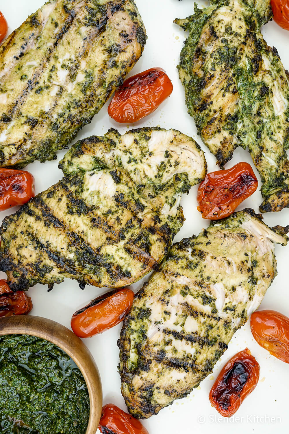 Pesto chicken with cherry tomatoes on a white baking sheet.