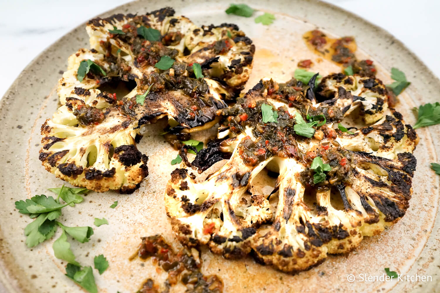 Cauliflower steaks served with chimmichurri on speckled gray plate.