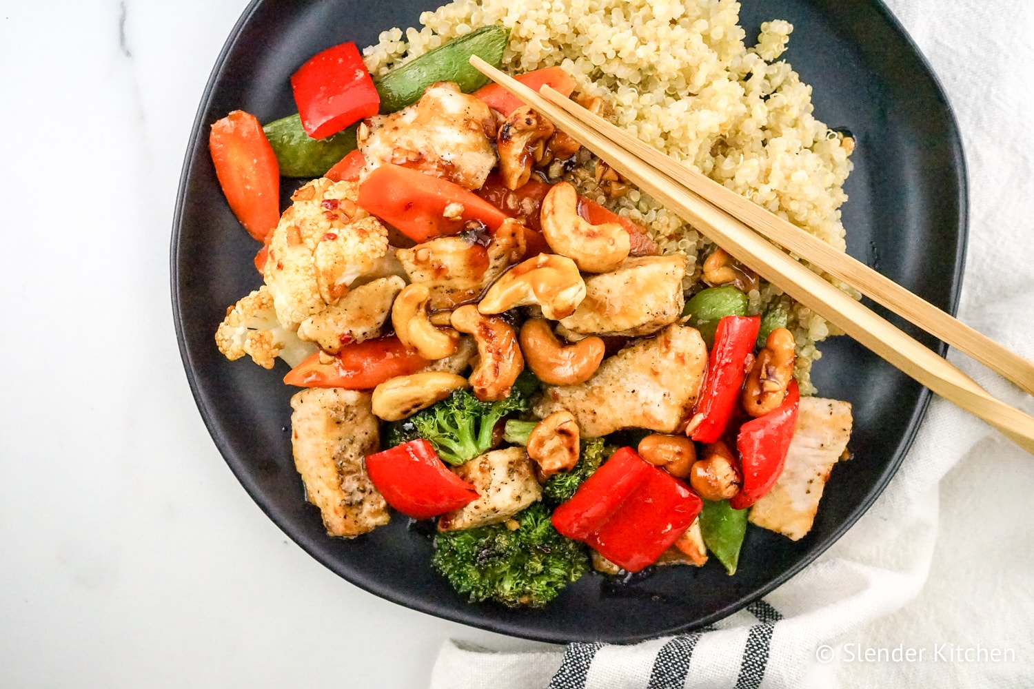 Healthy Cashew Chicken with Vegetables on a dark plate with chopsticks.
