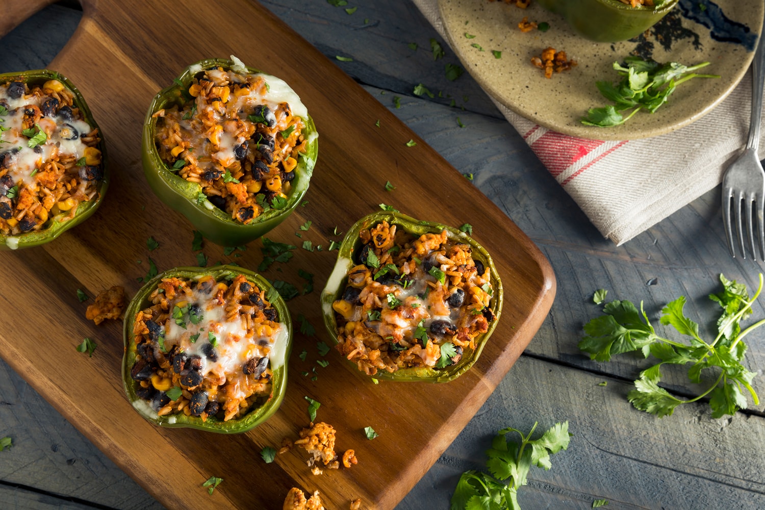 Vegetarian stuffed peppers with corn, black beans, and rice on a cutting board.
