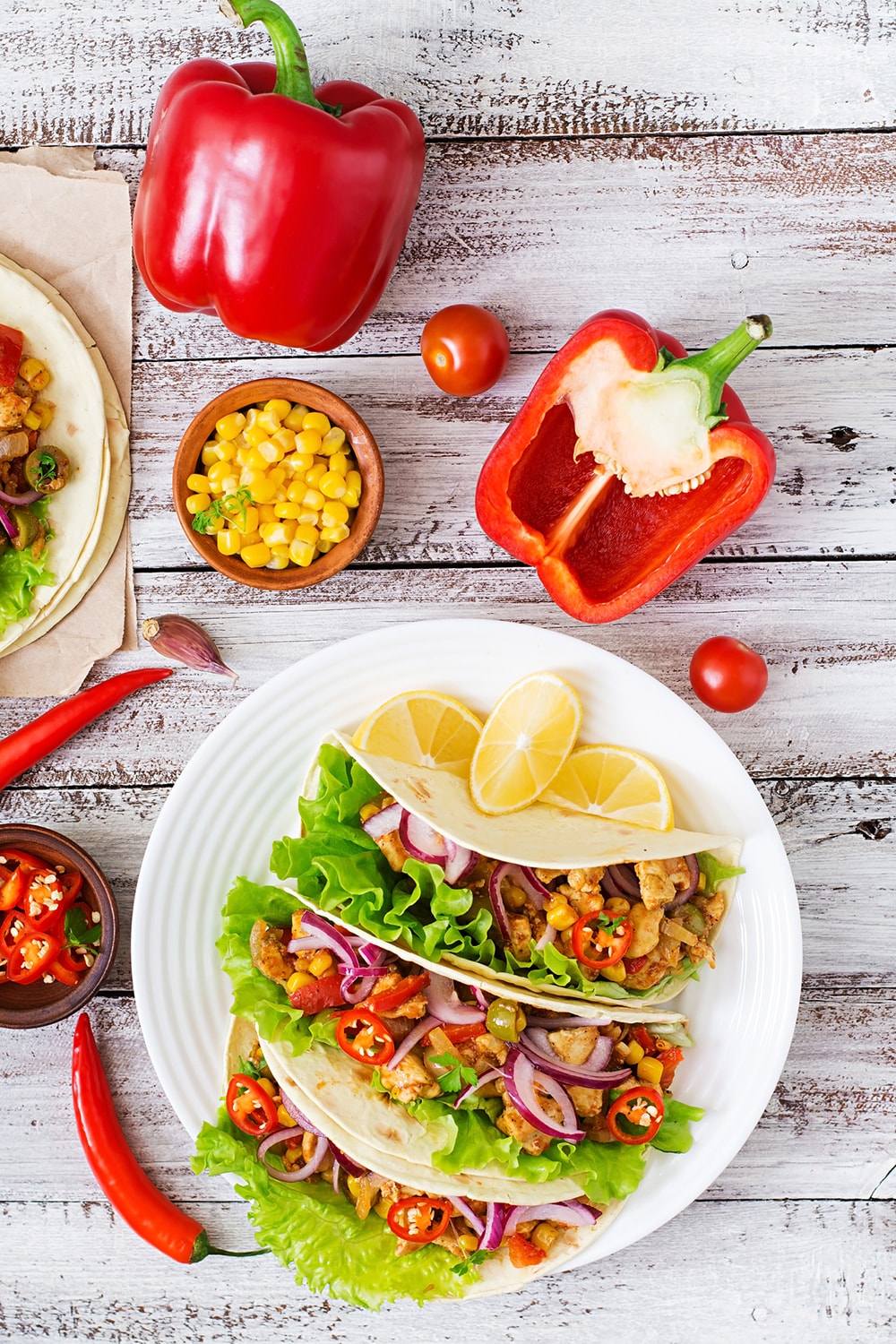Spicy Chicken Tacos with corn on a white background with fresh produce.
