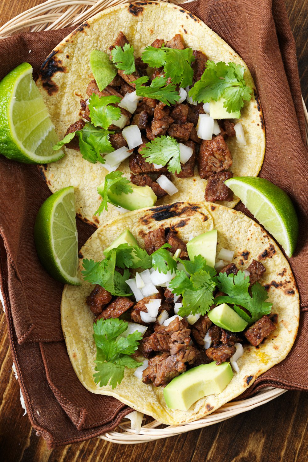 Two grilled steak tacos topped with cilantro and onion in a basket with a brown napkin inside 