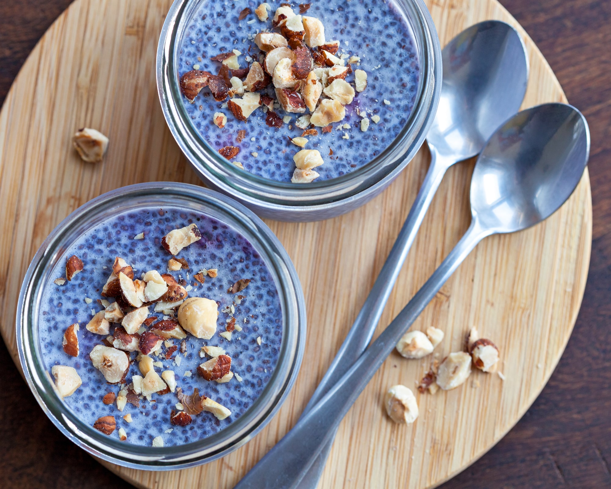 Two containers light Blue chia pudding on a wooden bar with a spoon.