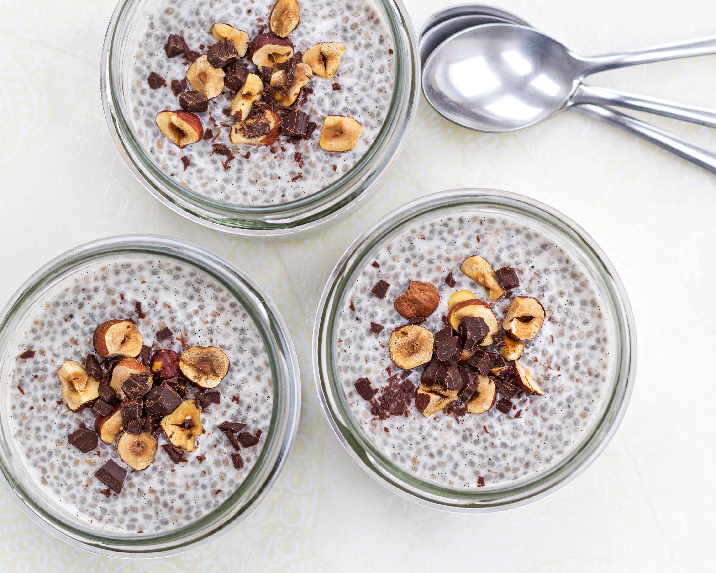 Three containers of chia pudding with nuts on top in mason jars.