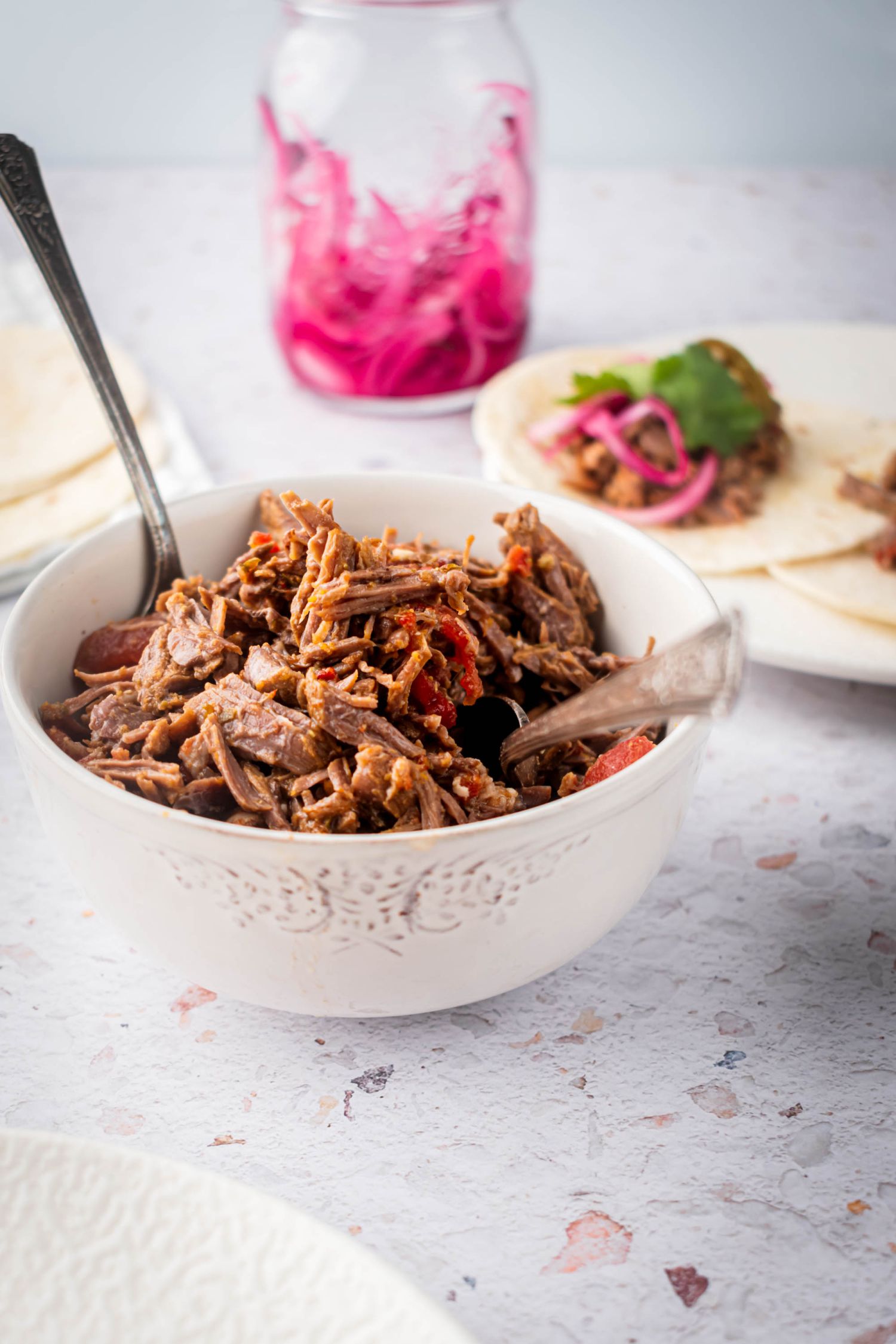 Shredded Mexican beef cooked in the slow cooker and served in a bowl with pickled red onions and wrapped in tortillas.