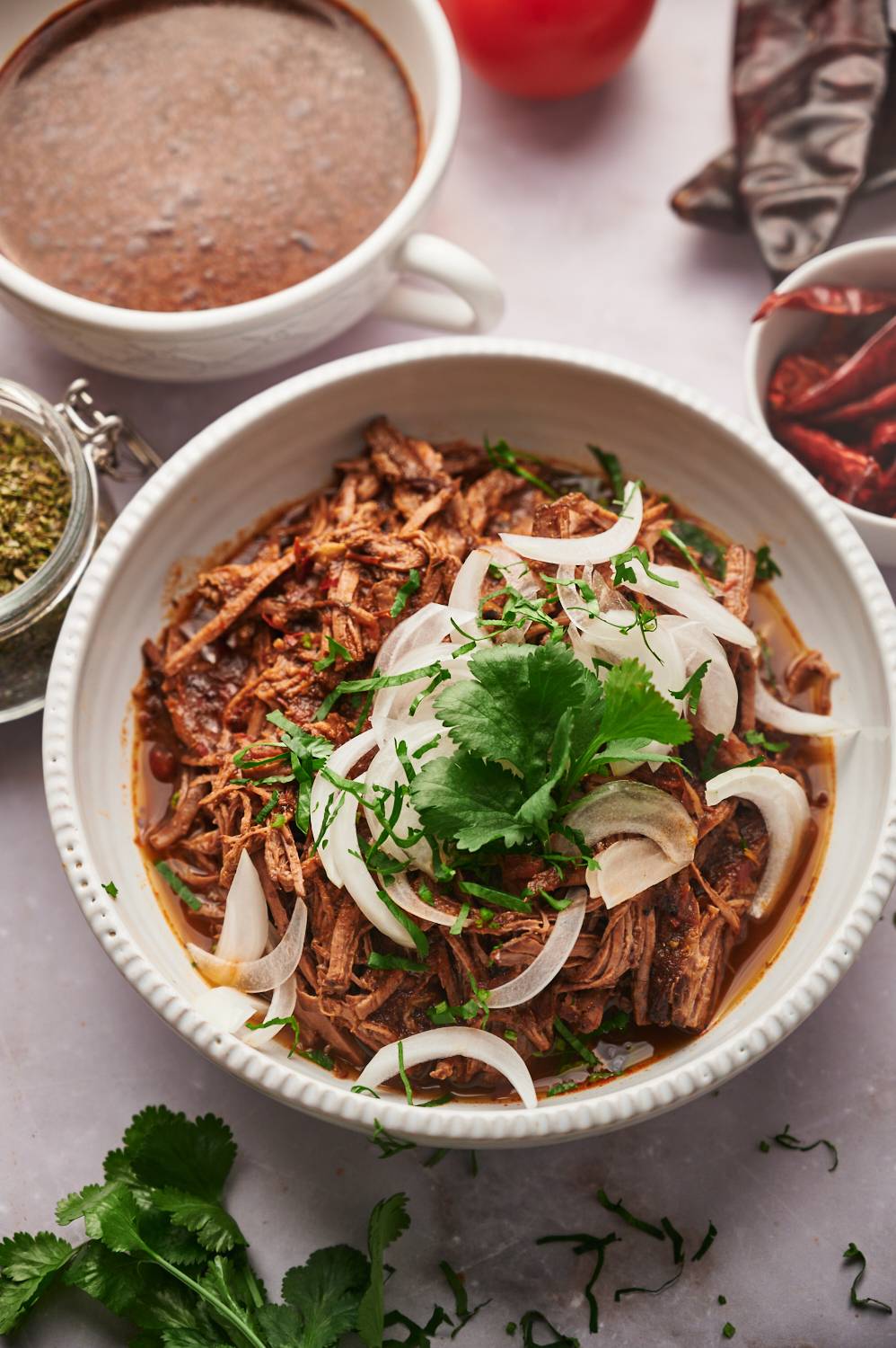 Beef birria in a bowl with a dried chili pepper sauce, white onion, and cilantro.