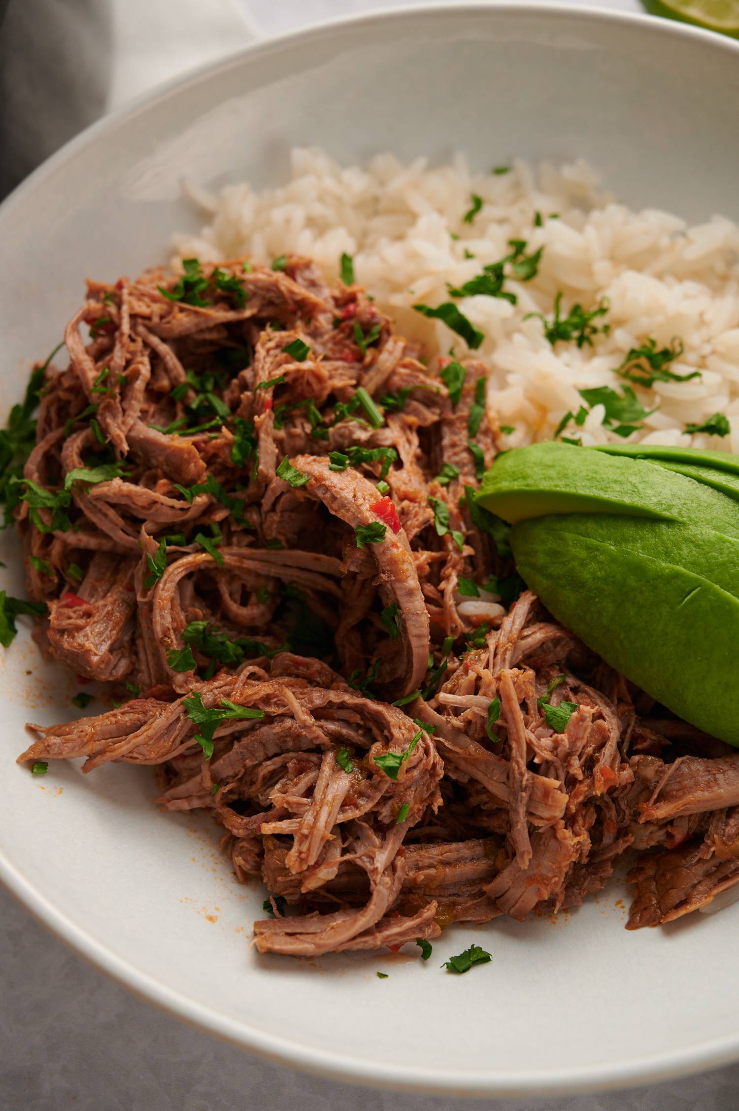 Shredded beef machaca served in a bowl with white rice, avocado, lime, and cilantro.