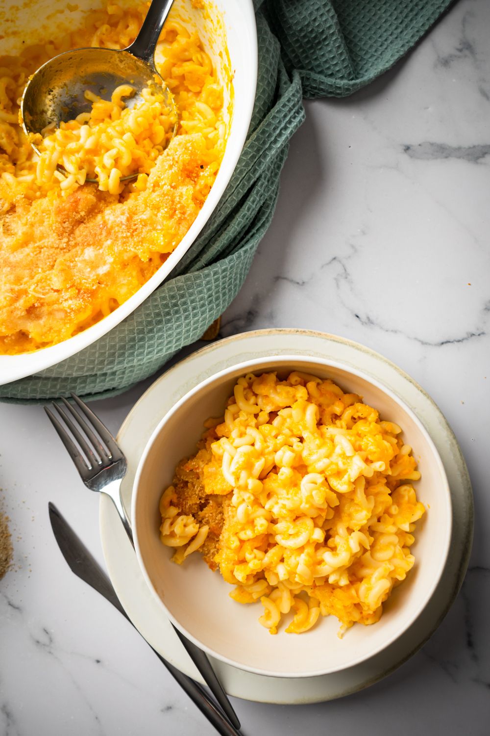 Cheddar macaroni and cheese with a creamy carrot and cheddar sauce in a bowl and in a baking dish.
