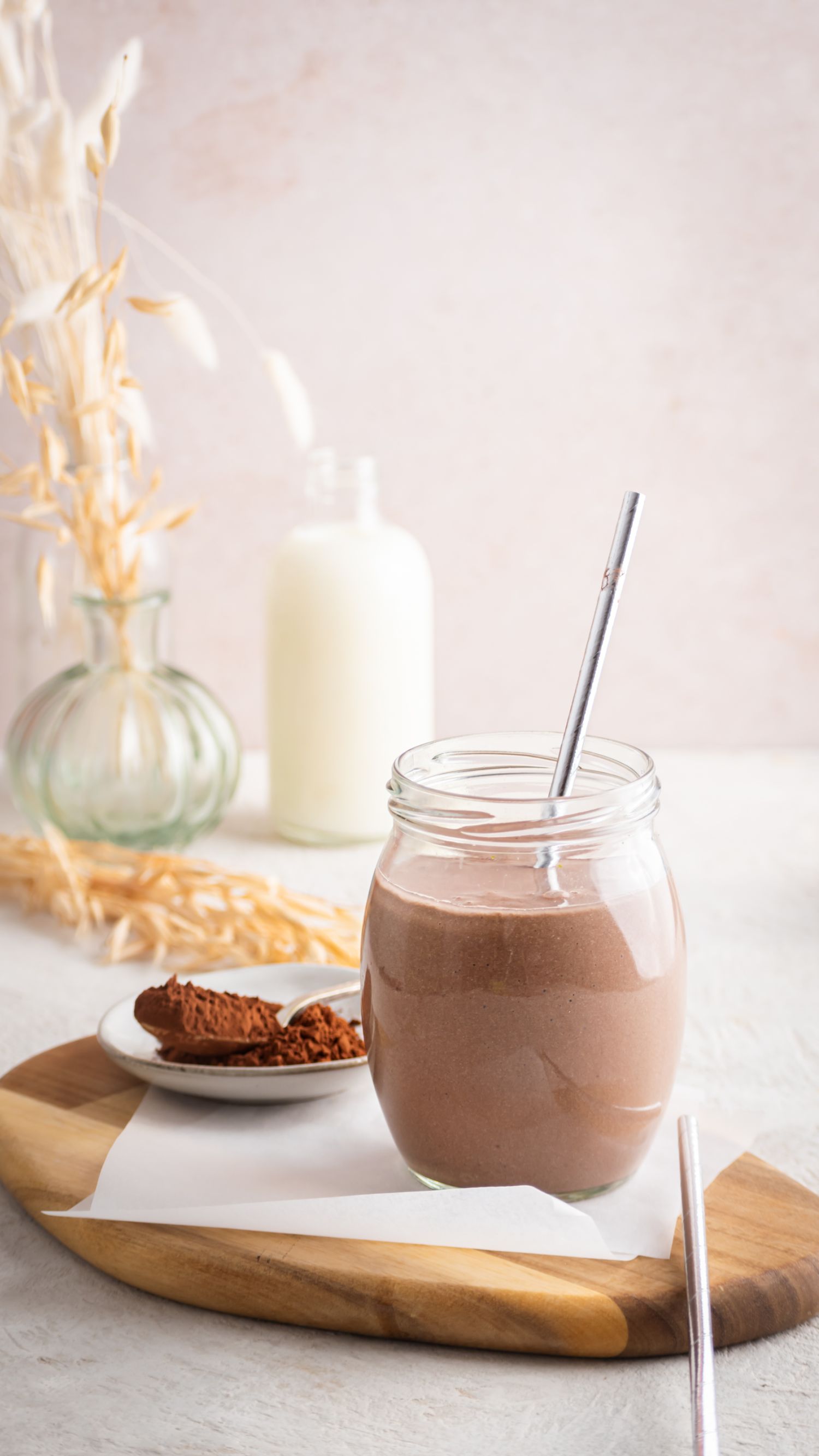 Glass filled with a chocolate breakfast shake with almond milk and cocoa powder on the side.