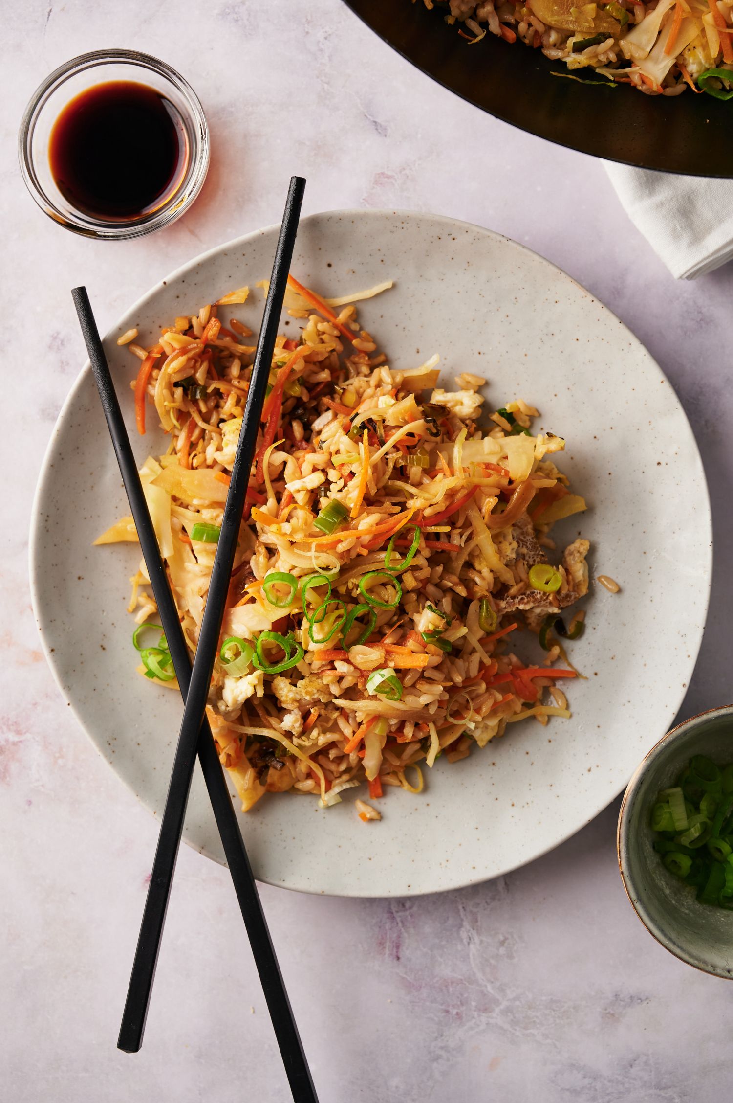 Fried brown rice and vegetables on a plate with chopsticks and soy sauce.