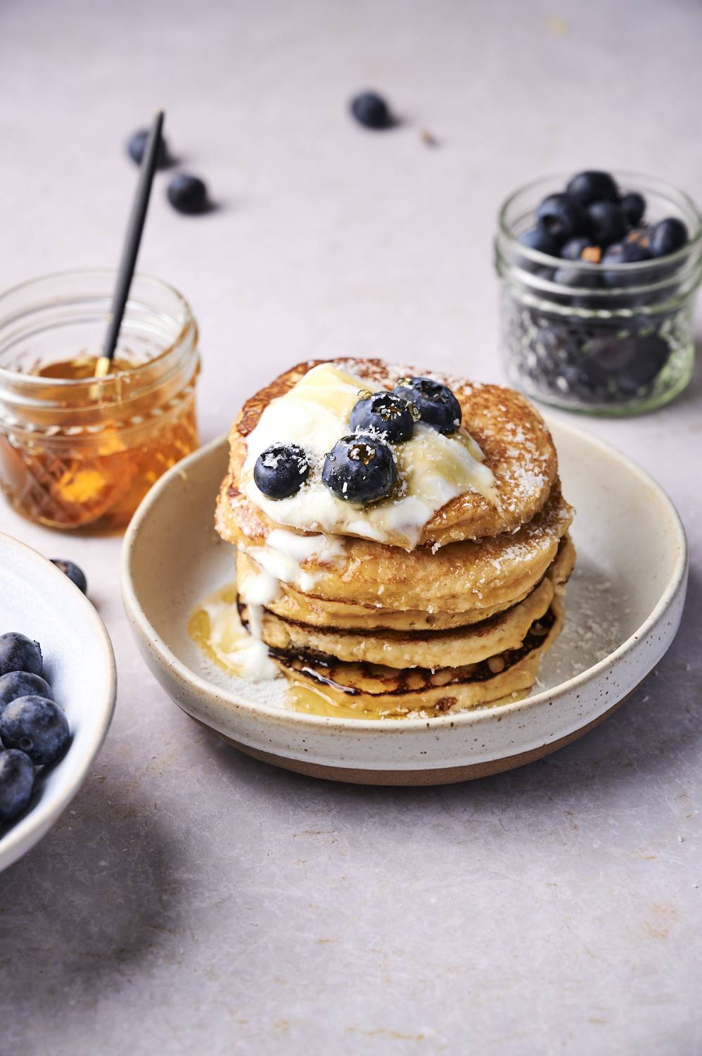 Keto almond flour pancakes stacked on a plate with plain yogurt, blueberries, and honey.