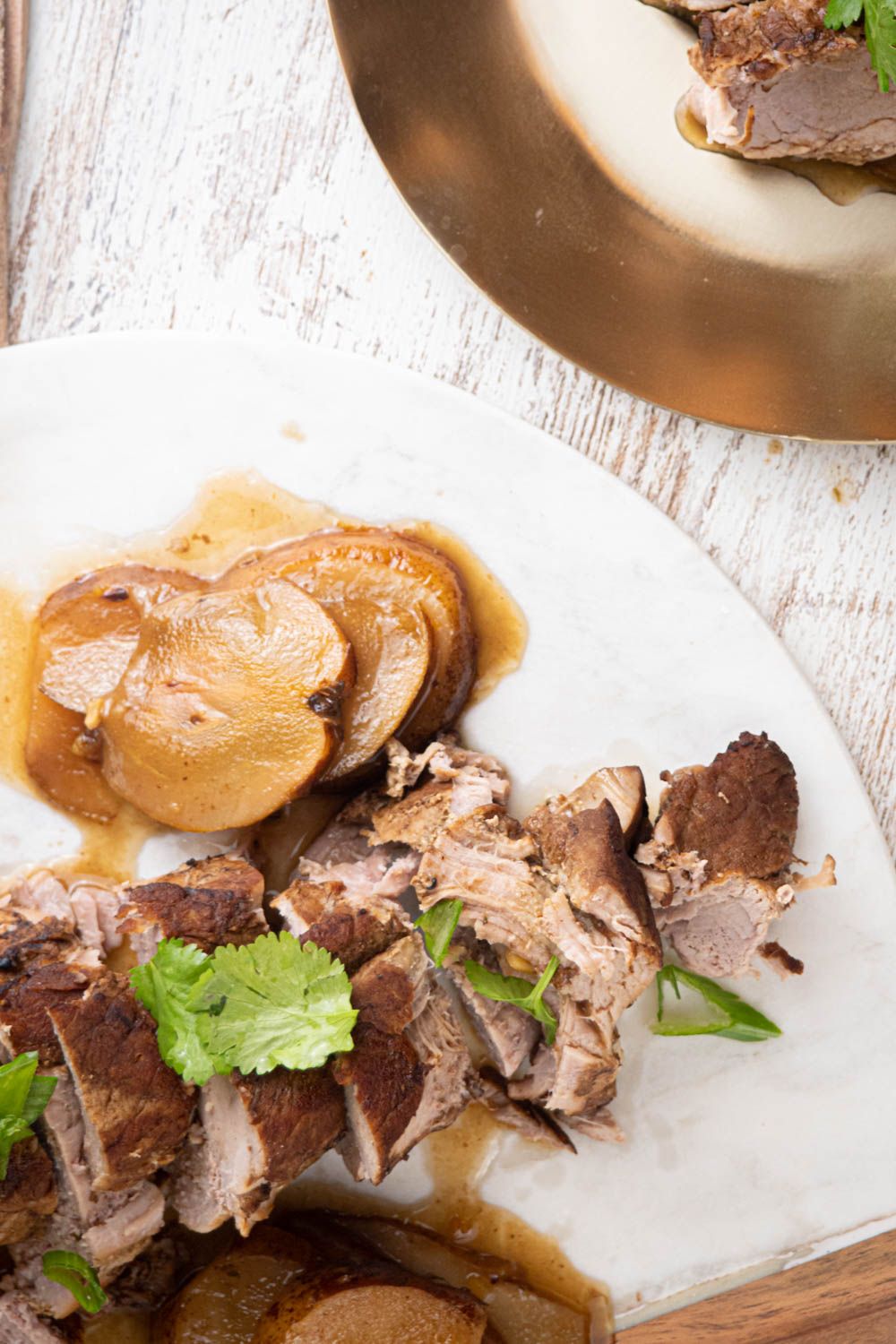 Crockpot pork tenderloin with honey, balsamic, and pear slices on a marble plate.