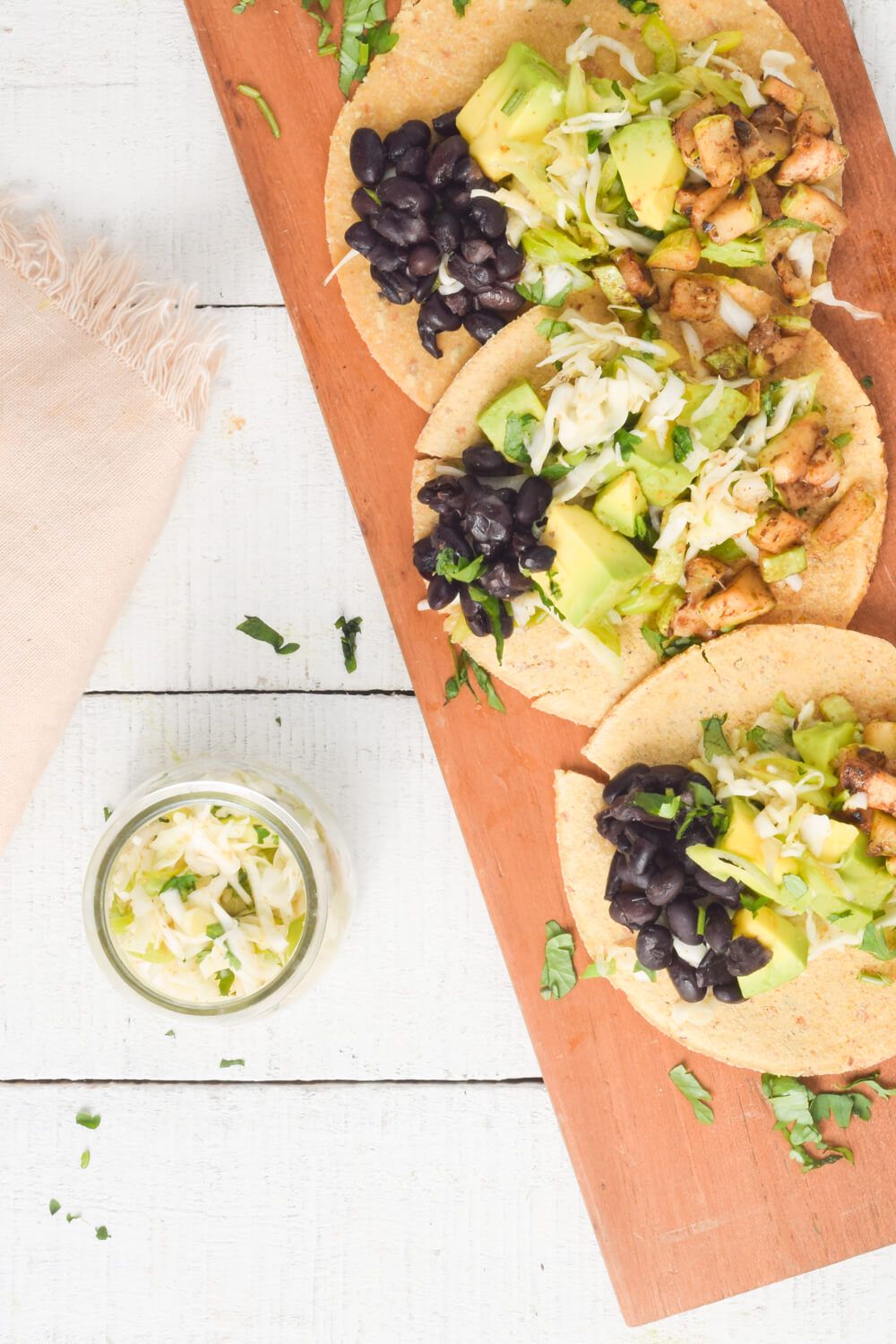 Three vegetarian black bean and zucchini tacos with cabbage slaw and avocado.
