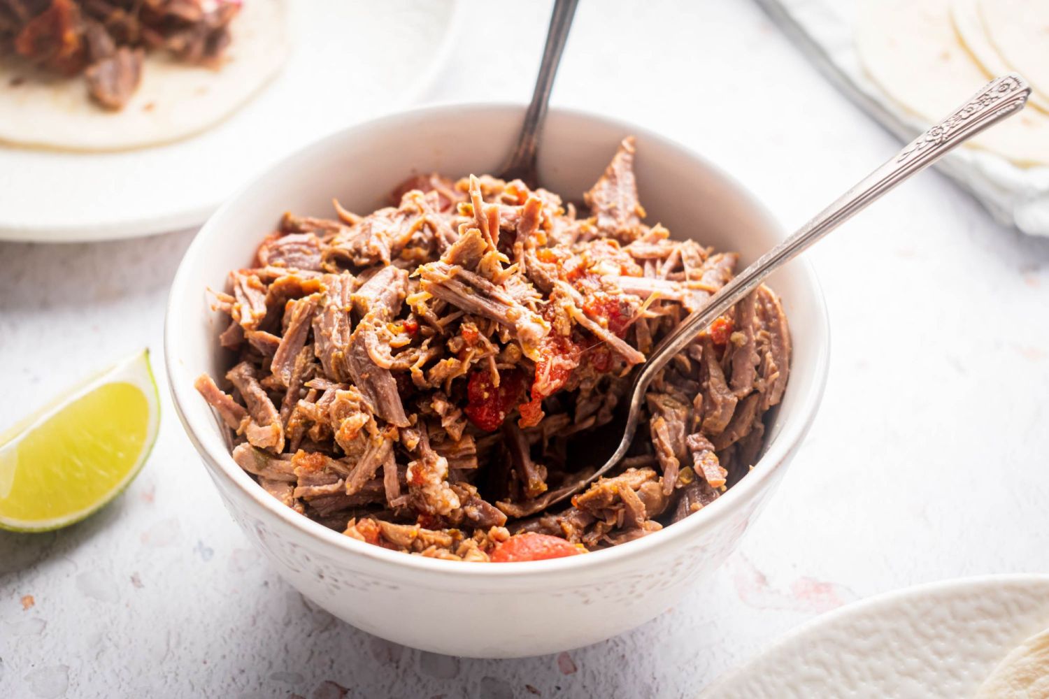 Easy crockpot Mexican shredded beef cooked with tomatoes, spices, and chipotle peppers in a bowl with a lime wedge.