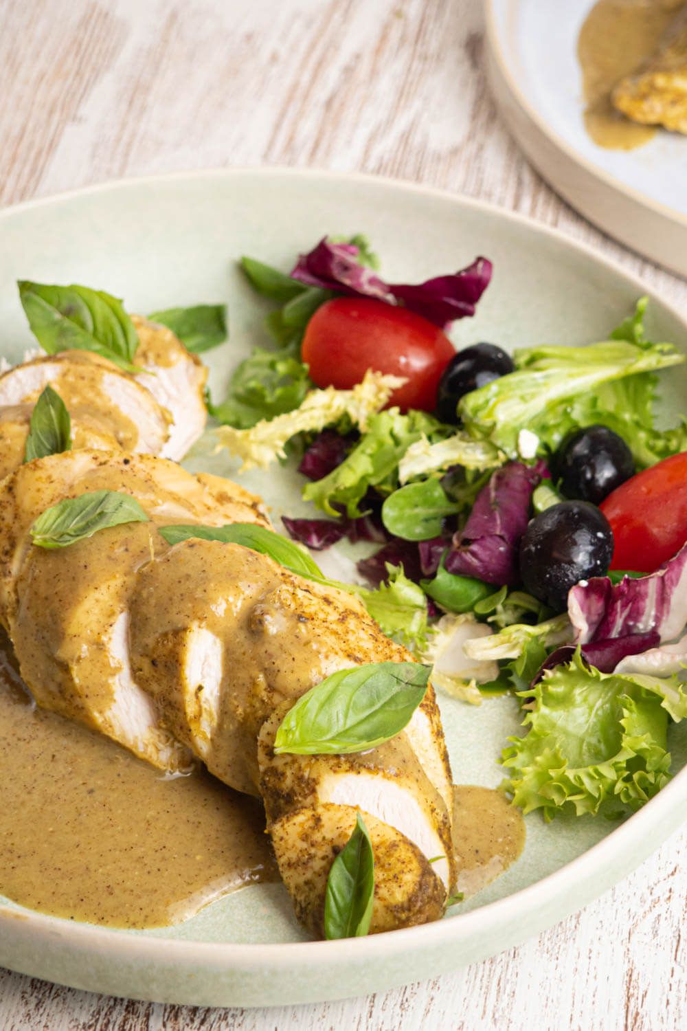 Crockpot coconut basil chicken breast cut into slices on a plate with a green salad.