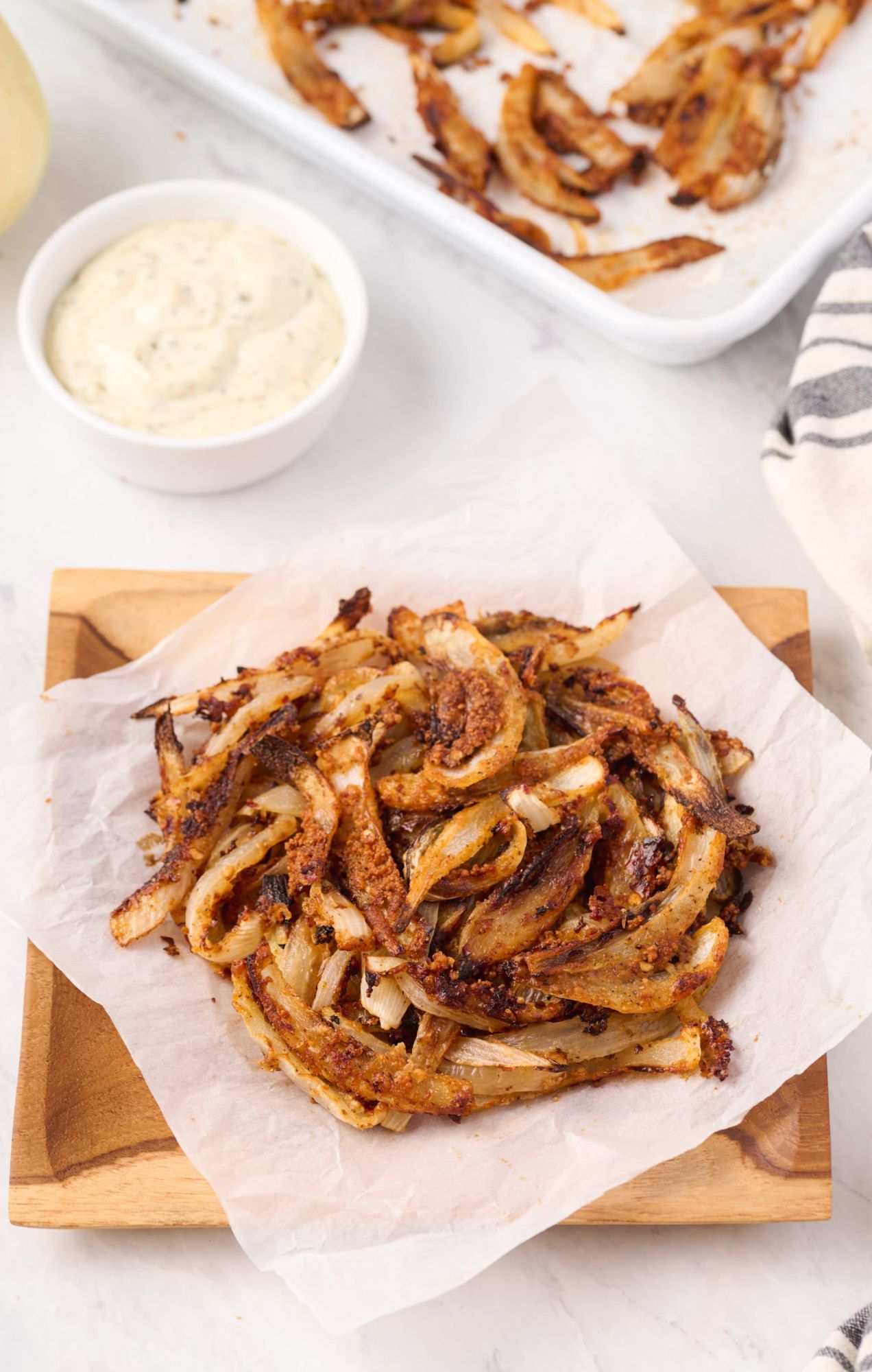 Crispy baked Parmesan onion straws in a bowl and on a baking sheet with parchment paper.