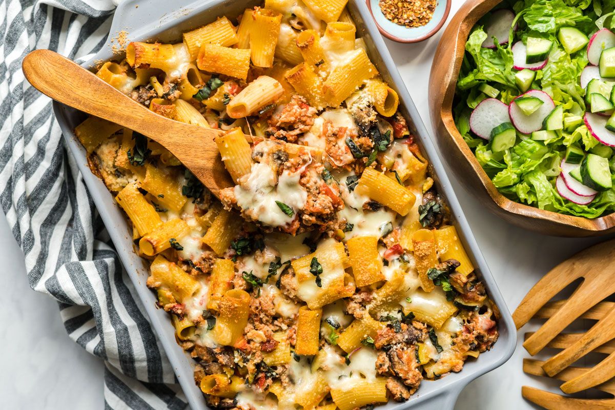 Baked ziti casserole with ground turkey and vegetables in a baking dish with salad on the side.