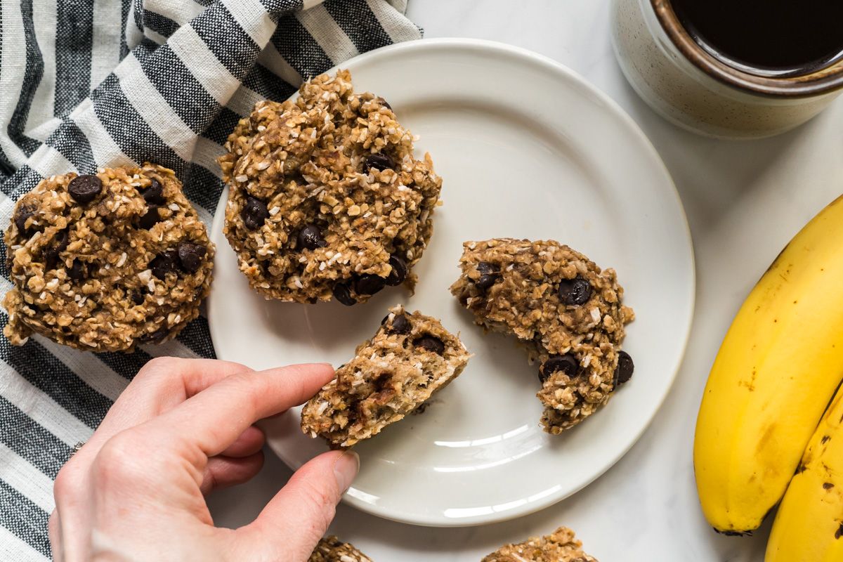 Banana oat cookies with chocolate chips on a plate with coffee and banana on the side.