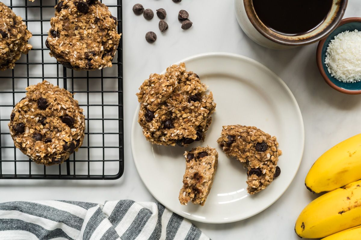 Banana chocolate chip oatmeal cookies with rolled oats and banana on a rack and plate.