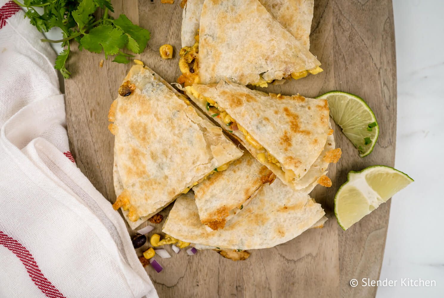 Freezer breakfast quesadillas with eggs, black beans, onions, and taco seasoning on a cutting board with cilantro.