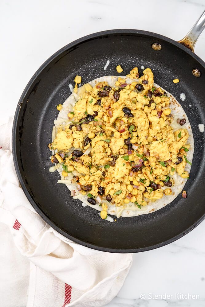 Breakfast quesadillas in a pan with eggs, beans, corn, cilantro, onion, and taco seasoning.