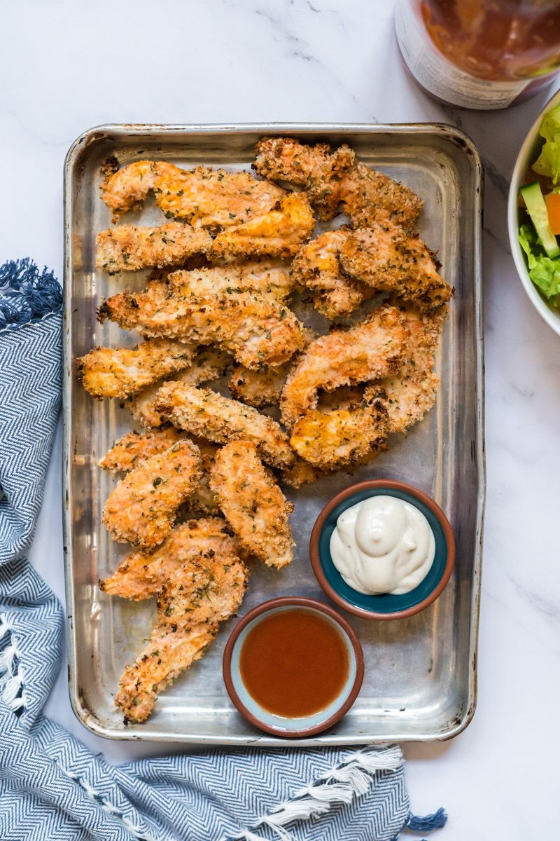 Ranch buffalo chicken strips on a baking dish with crispy breading and served with ranch dressing and buffalo sauce.
