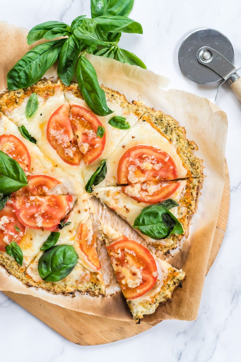 Cauliflower pizza crust cooked with melted cheese, tomato slices, and basil.