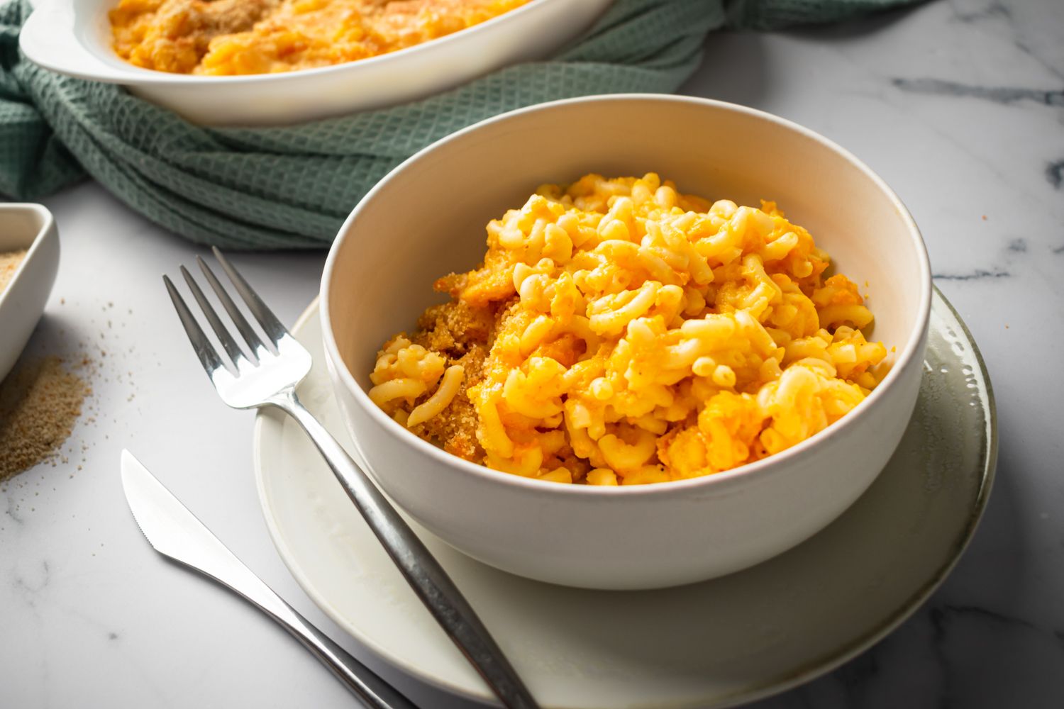 Vegetable macaroni and cheese made with carrots and cheddar cheese in a bowl with a fork and knife.