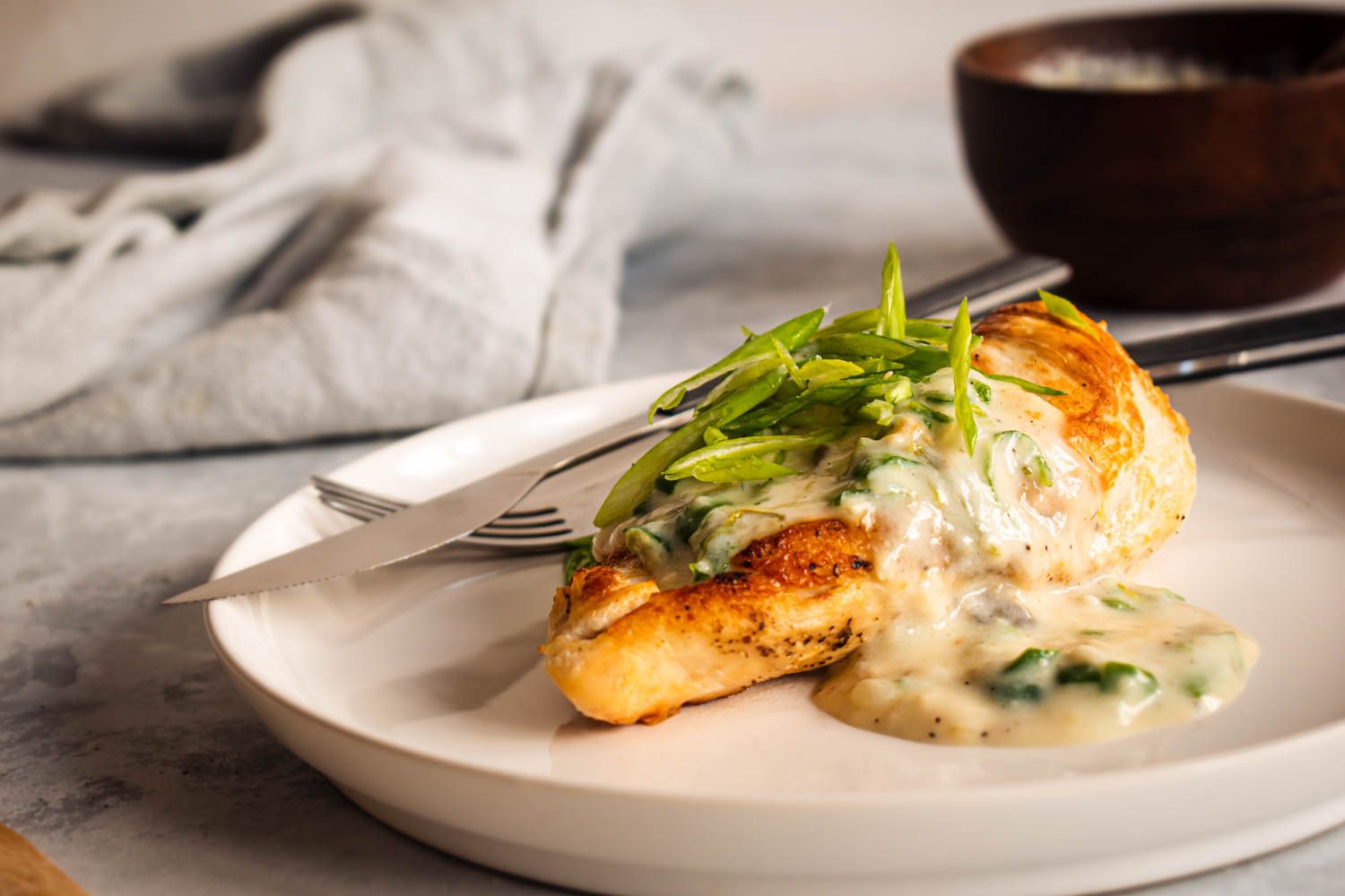 Chicken breast with a crispy brown exterior topped with creamy jalapeno sauce and sliced green onions.