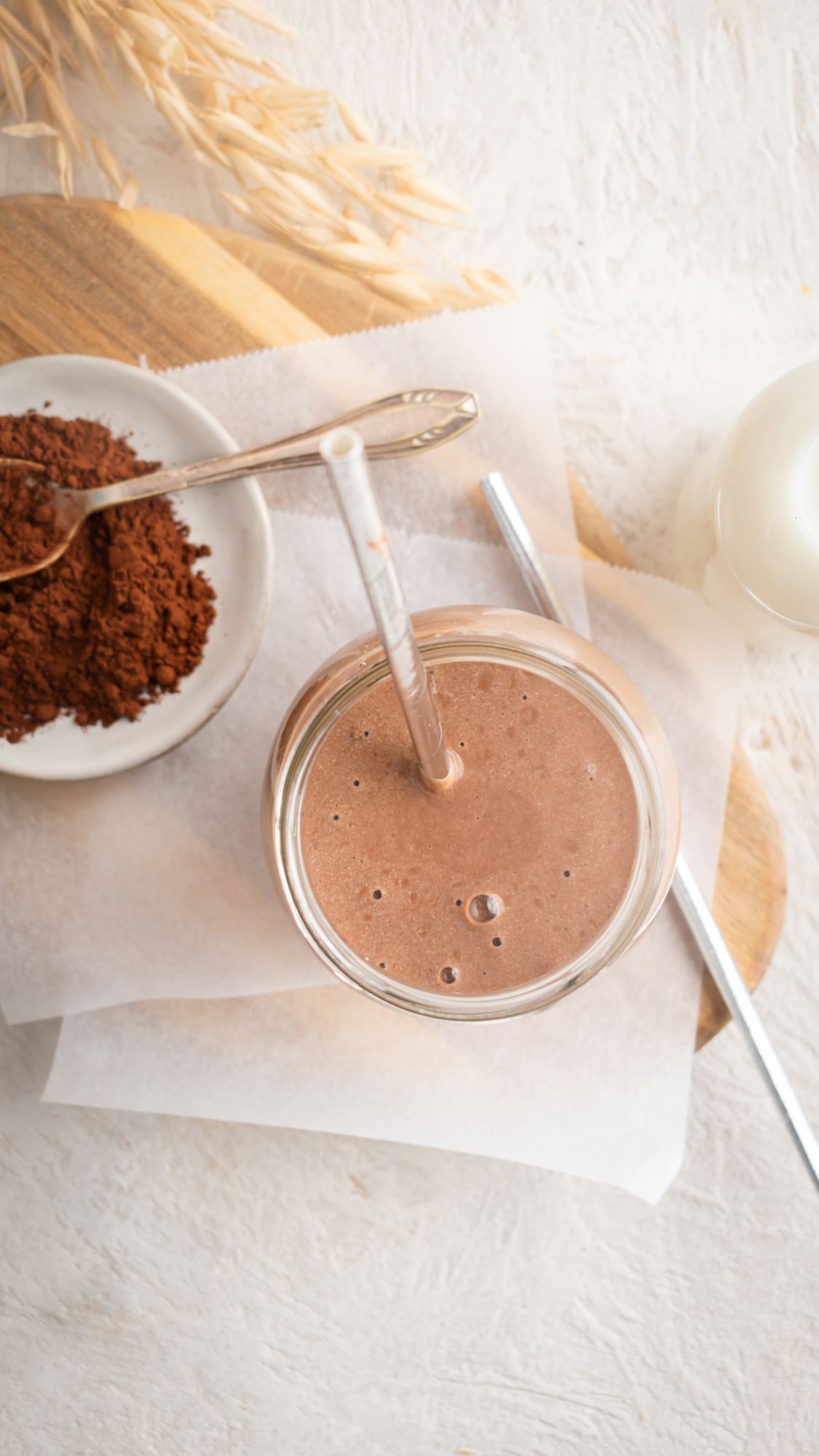 Chocolate protein shake served in a glass with a metal straw and cocoa powder on the side.