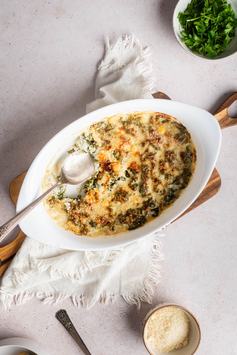 Kale cooked in cream sauce with crispy Parmesan cheese in a baking dish with two spoons.