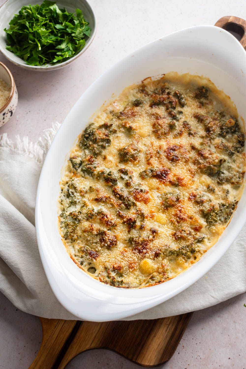 Baked creamed kale with a crispy topping in a baking dish with kale and Parmesan on the side.